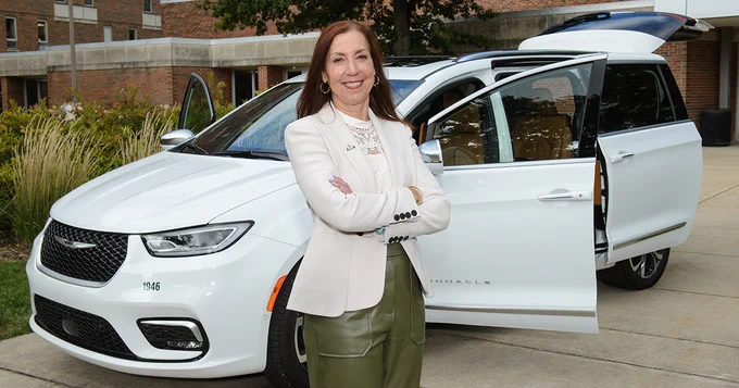 Chris Feuell wearing white blazer with arms crossed smiling at camera standing in front of white Chrysler safe ride van.