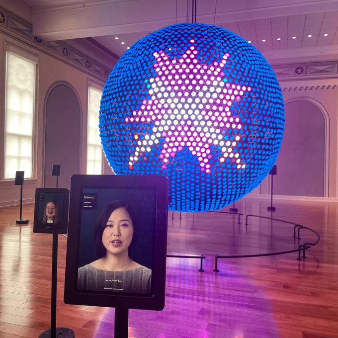 A tablet with Korean language ambassador Shiwon in front of the Spoken World globe at Planet Word, which is activated with an animation of two swords crossing on a pink explosive background.