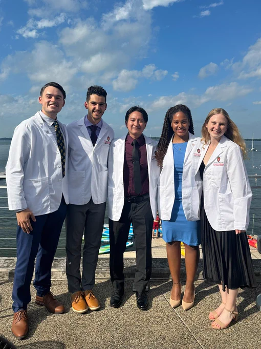 5 students gathered together in white coats in front of Lake Mendota