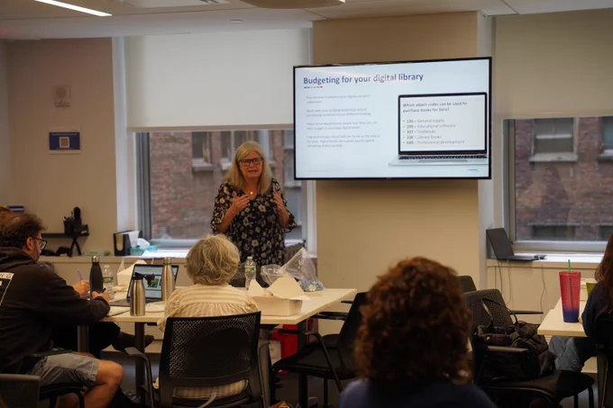 This photo shows someone standing at the front of a classroom doing a training for new librarians.