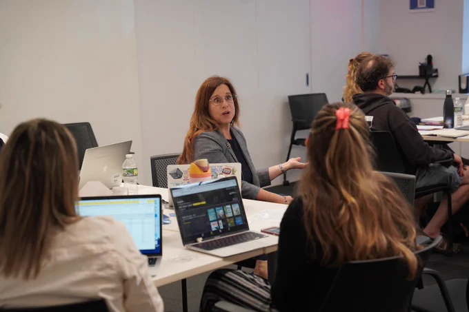 This photo shows someone sitting at a table speaking to other people in the room at a training for new librarians.