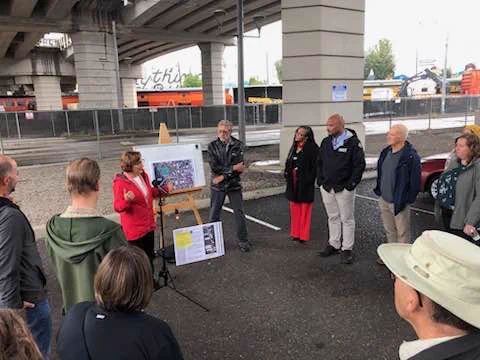 Congresswoman Bonamici stands next to a map on an easel as she speaks to a crowd gathered under a bridge adjacent to railroad tracks in the Central Eastside.