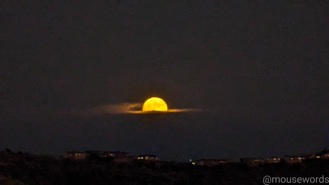Half of a full moon rising out of a storm cloud