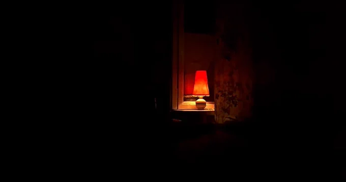 A small lamp glows orange in a dark room