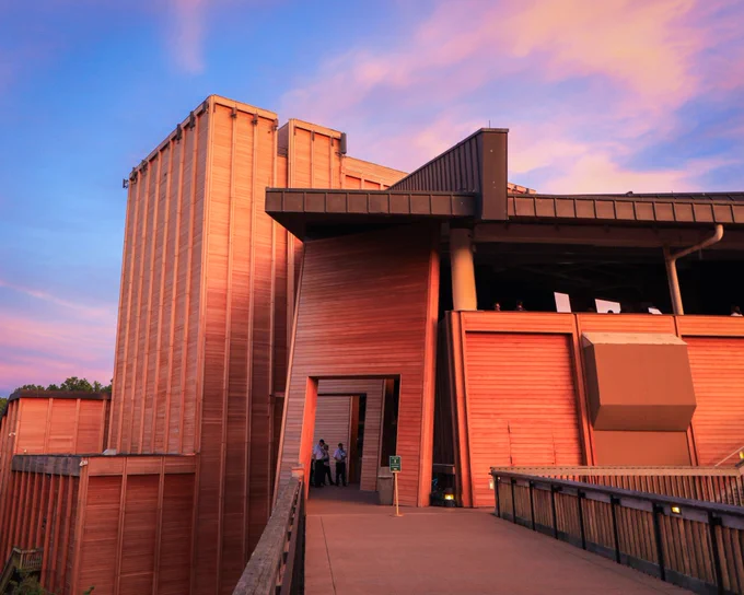 A large wooden amphitheater is framed beneath a purple sunset.