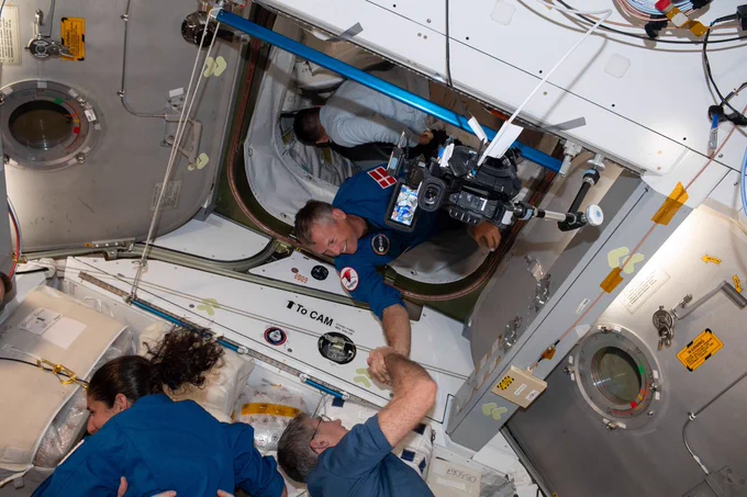 ESA astronaut Andreas Mogensen arrives at the International Space Station. He is wearing his blue flightsuit and welcomed with a handshake.