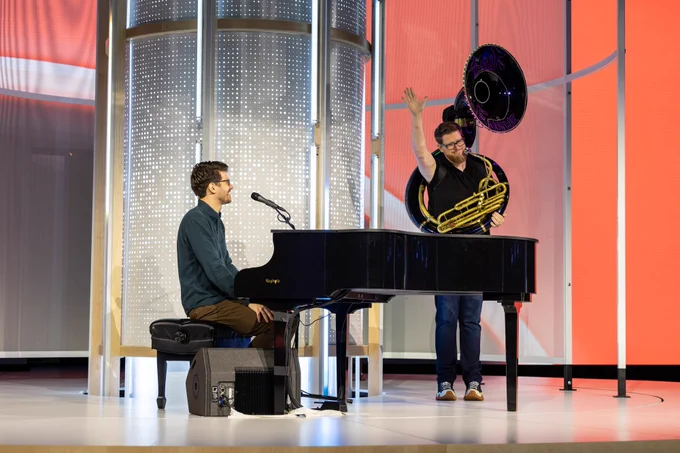 A photograph of Forrest Brazeal playing the piano and Miles Ward playing the electric sousaphone on stage at Google Cloud Next. 