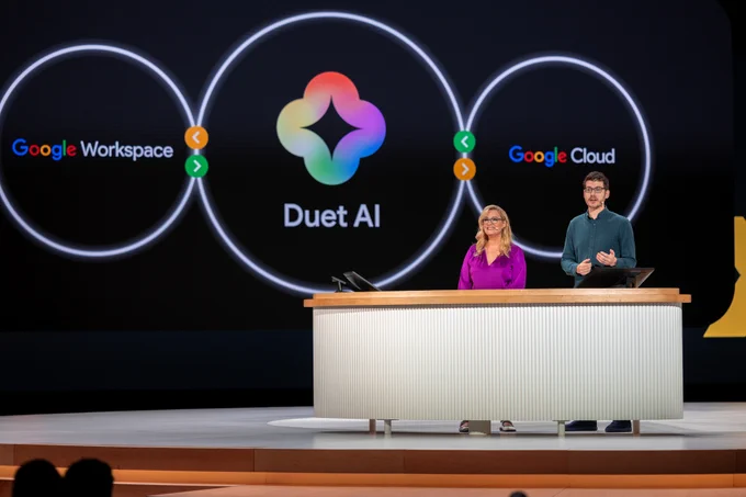 A photograph of Alice Keeler and Forrest Brazeal on stage at Google Cloud Next. The image behind them shows the Duet AI logo between 'Google Workspace' and 'Google Cloud.' 