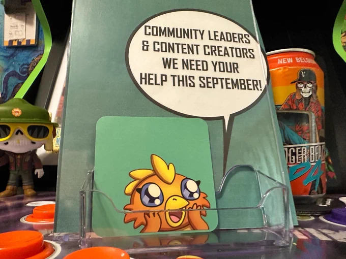 a photo of an acrylic display holding a small square card with the Steven Spohn cartoon chicken character on it and behind it a larger card with a thought bubble containing text that says 'Community leaders & content creators we need your help this September!'