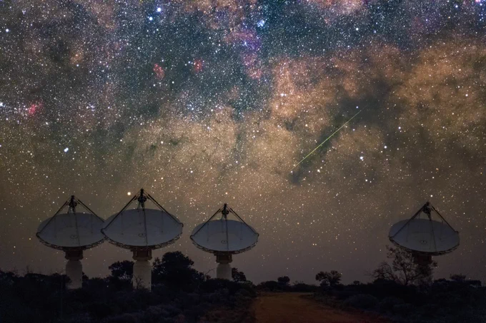 Four dish-like antennas pointing to the sky. The night sky is filled with stars and clouds.