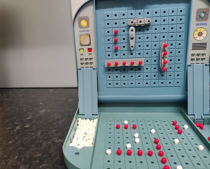 Old fashioned battleships game, half completed with red pegs stuck in half the ships