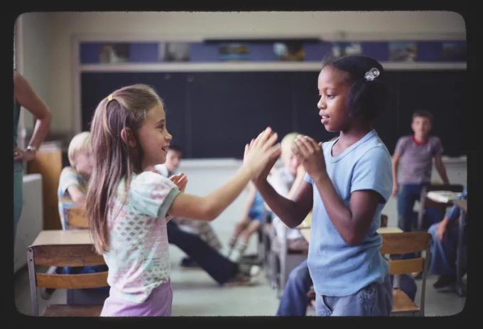 Two girls playing hand clap games in the classroom. 