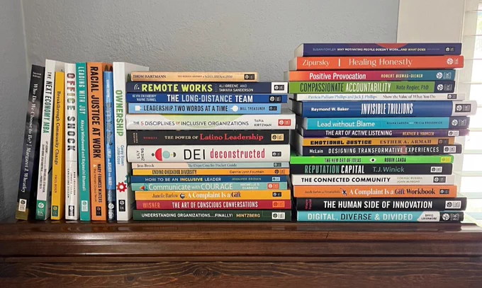 Dozens of BK books are stacked high in three piles on top of a bookcase.