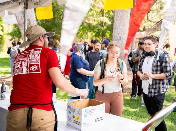 UNM students on the right receive ice cream from a member of UNM's leadership team, shown in a red UNM shirt, at UNM President Stokes's Ice Cream Social.