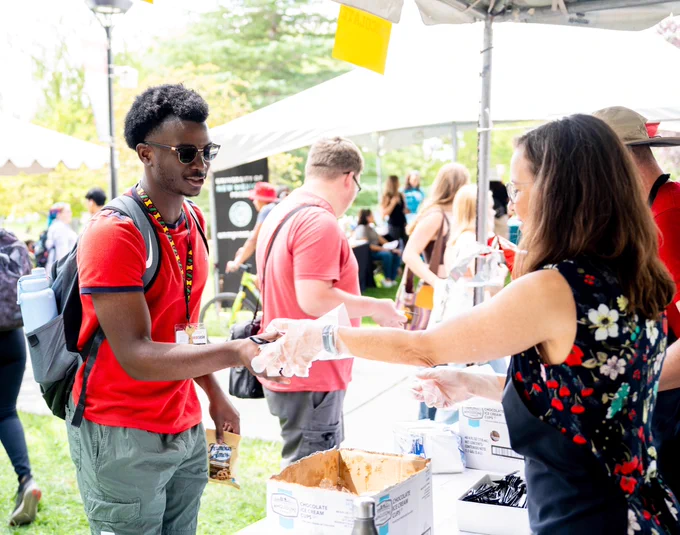 UNM staff, at right, hand ice cream to a Lobo student, wearing amazing sunglasses and dressed in a red short-sleeved shirt.
