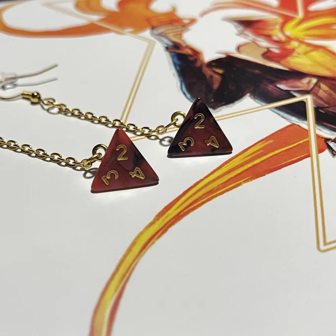 A pair of red, black, and gold mini d4 earrings with The Dictator page of the Die RPG manual as a background.