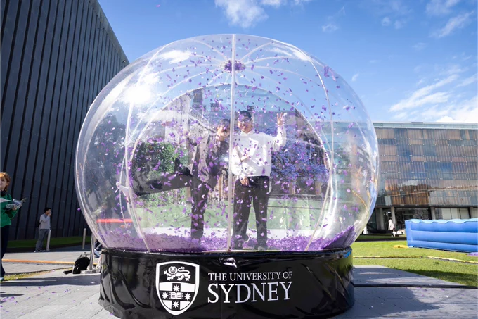Students in snow globe bubble with purple confetti flying around, the black base has The University of Sydney logo