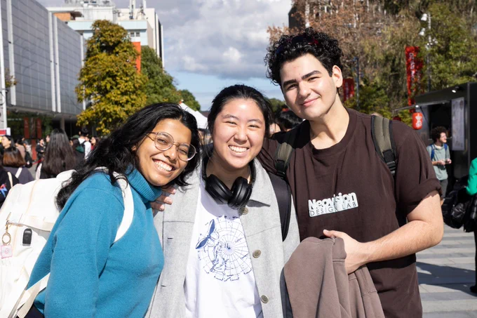 three students smile at camera in hoodies and t shirts
