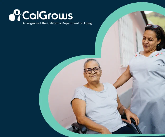 A middle-aged Latina smiling at an elderly Latina with glasses in a wheelchair. 