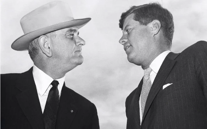 Photograph of Lyndon Johnson in a cowboy hat staring down JFK 