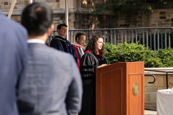 Photo Interim University Chaplain Maytal Saltiel behind a brown, wooden podium delivering a benediction at the Yale Graduate School of Arts and Sciences matriculation ceremony.