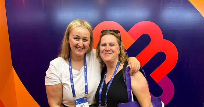 Midwifery student Meghan Critchlow and Dr Amanda Firth wear purple lanyards and smile together in front of a large purple sign at the  International Confederation of Midwives (ICM) Congress 2023 in Bali.