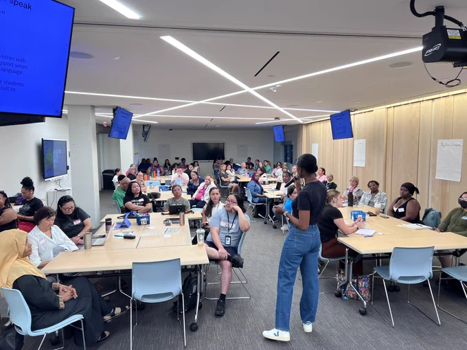 A group of about 55 individuals seated at tables in a training room listening to a presenter.