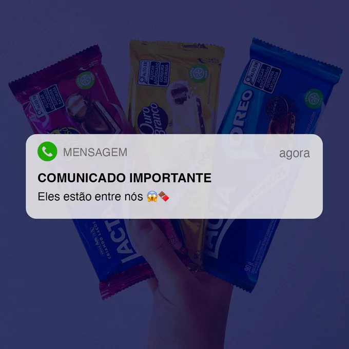 Imagem de um pop-up de mensagem escrito:​
COMUNICADO IMPORTANTE​
Eles estão entre nós 😱🍫​

E como imagem de fundo temos os três tabletes recheados de Lacta, da esquerda para a direita: Sonho de Valsa, Ouro Branco e Oreo.