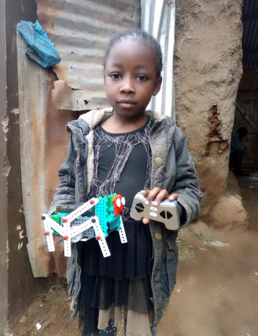 A Kenyan girl in the Nairobi slum holding a remote controlled robot 