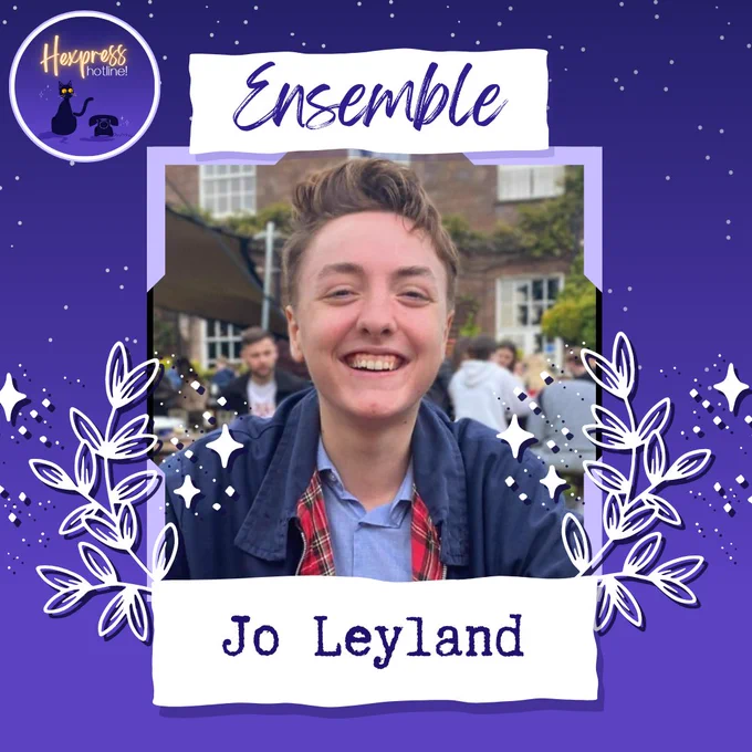 A photo on a purple background of a person with short brown hair, wearing a light blue shirt and dark blue jacket. In the top left corner is the Hexpress Hotline logo with a black cat and an old phone. Above the headshot is the label "Ensemble" in cursive writing.  Underneath the headshot are the words "Jo Leyland", and around the headshot are white leaves and stars.