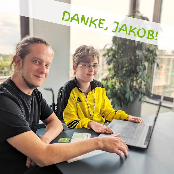 Ein Mann und ein Junge im Rollstuhl sitzen an einem Tisch mit einem Laptop.