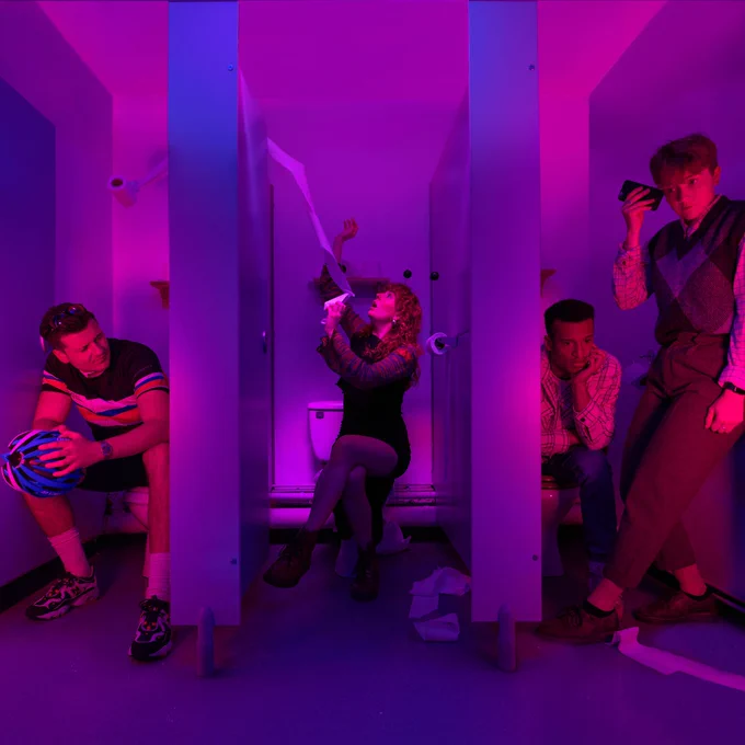Four figures in toilet cubicles, there is a purplish neon hue to the photo.