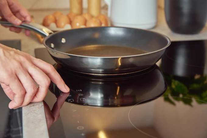 A close-up of a hand turning on an induction cooktop.