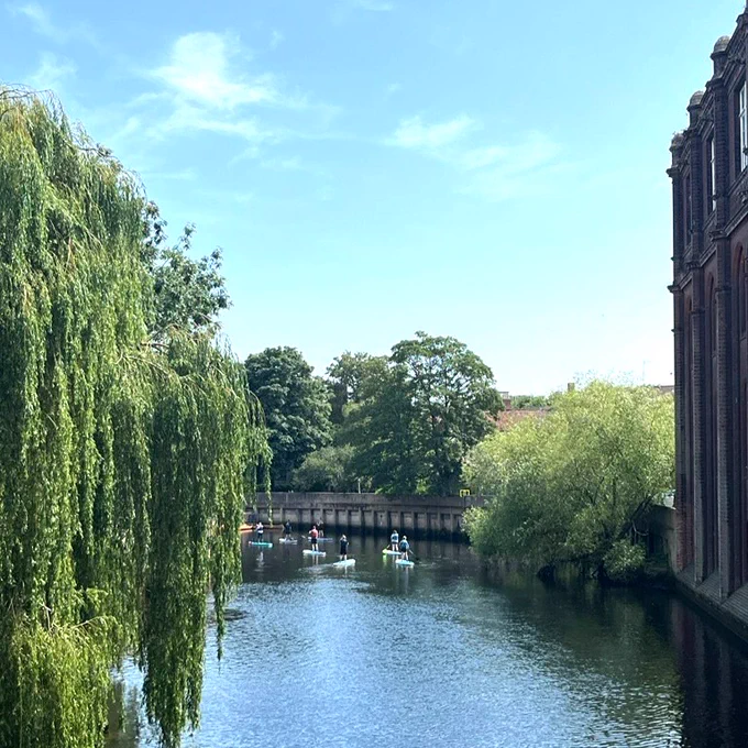 The river in Norwich with a blue sky as people paddle board on the river