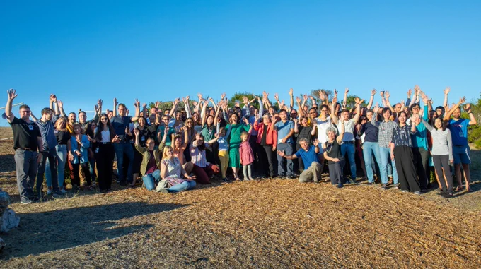 100  members of the T2T consortium stand together in a field at UC Santa Cruz, with hands raised in celebration.