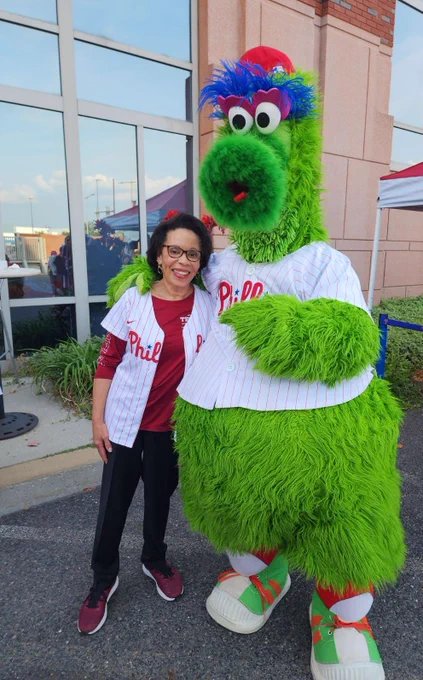 JoAnne Epps stands next to the Phillies Mascot while both wearing a Phillies jersey