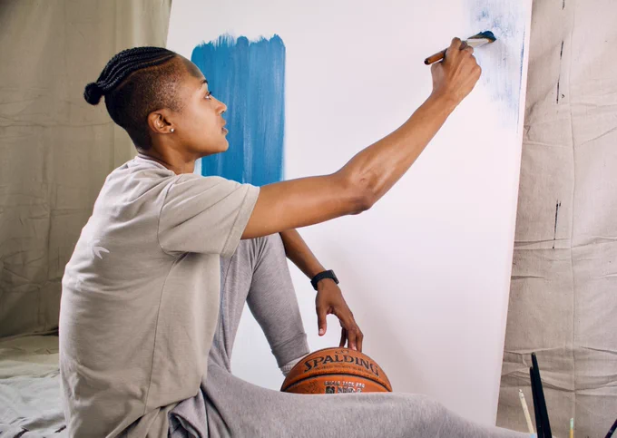 person sitting down painting whilst touching a basketball