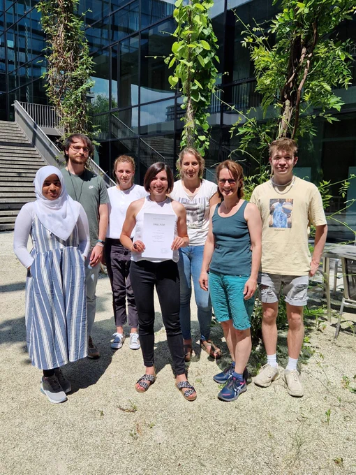 Isa is holding the certificate (Urkunde) of her new junior professor position (W1 tenure-track) surrounded by the Evolution of Plant Signaling Lab members: Sameena, Fran, Rania, Martha, Uli and Julian. They are standing in the courtyard of the ZMBP (Tübingen, Germany) under the bright sun.