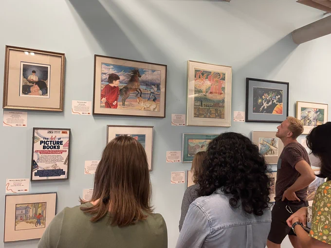 A group of people look at a small collection of original children's book illustrations at CSI Annex.