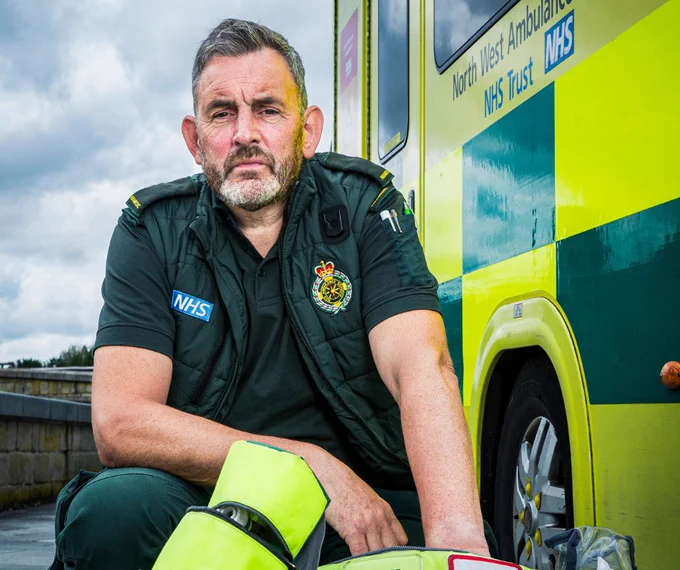 Paramedic Ian kneeling in front of a kit bag and next to an ambulance.
