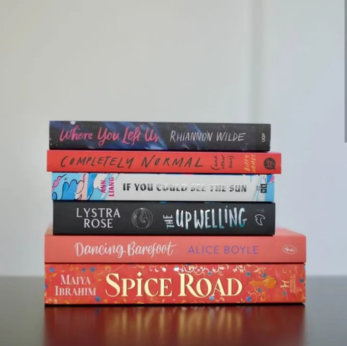 A stack of shortlisted books, including 'Where You Left Us' by Rhiannon Wilde , 'Completely Normal (and Other Lies)' by Biffy James, 'If You Could See the Sun' by Ann Liang, 'The Upwelling' by Lystra Rose, 'Dancing Barefoot' by Alice Boyle, and 'Spice Road' by Maiya Ibrahim.