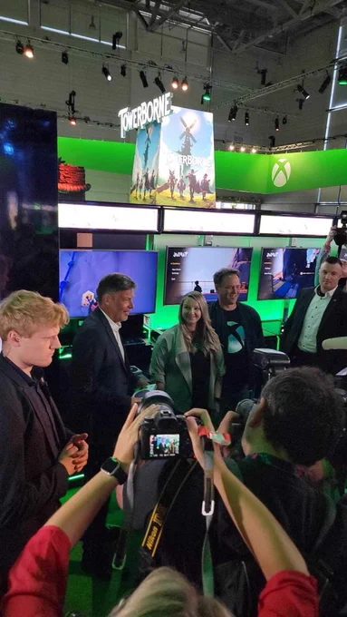 Kaitlyn at Gamescom standing in between Phil Spencer and the Vice Chancellor of Germany who is speaking to the press.