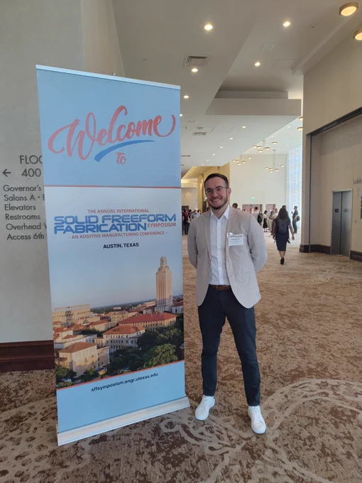 A business man stands next to a conference banner in a conference center hallway.