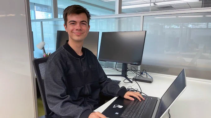 Richie Motorgeanu, learning resource development assistant for the Sherman Centre, can be seen sitting at his desk while smiling at the camera.