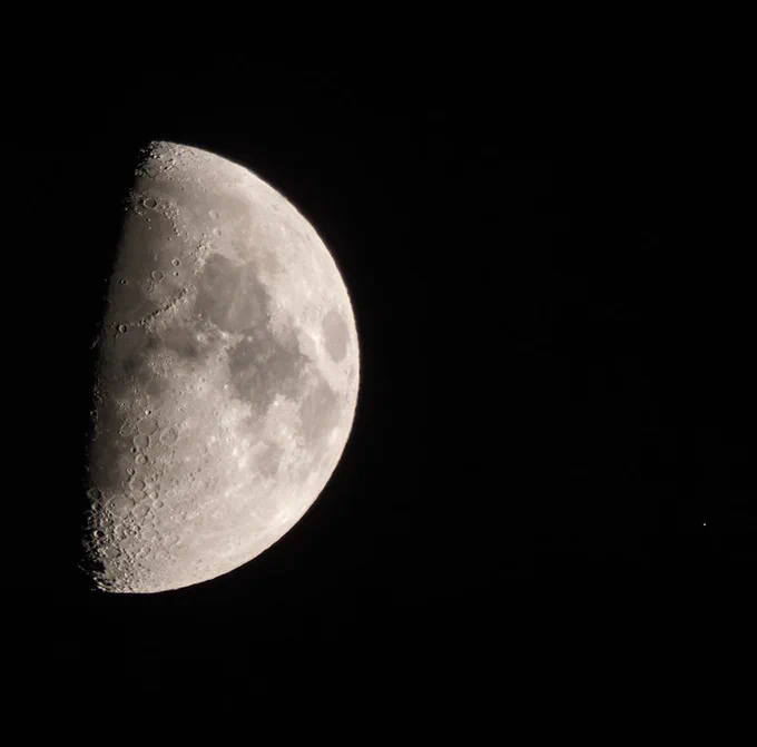 Half illuminated Moon passing in front of reddish Antares in the constellation Scorpius.