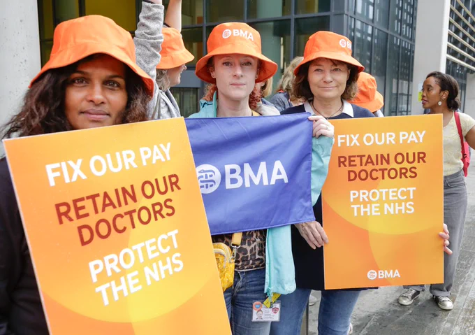 A group of female consultants on a picket line wearing orange BMA hats and holding placards