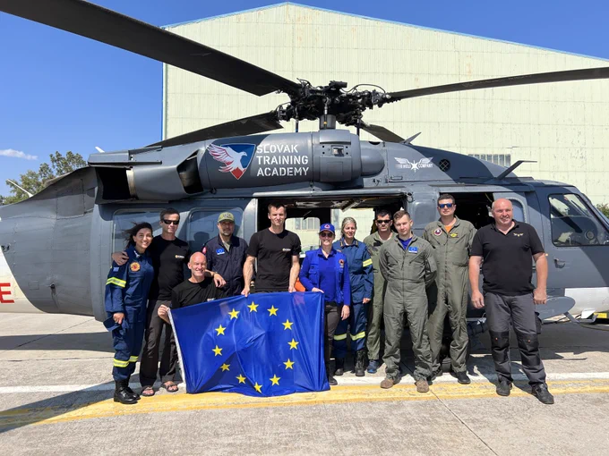 A Slovak firefighting team poses with an EU flag in front of a helicopter.