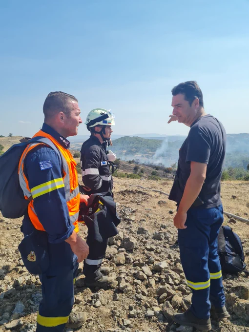 Three firefighters against the background of haze hovering over a burning forest.
