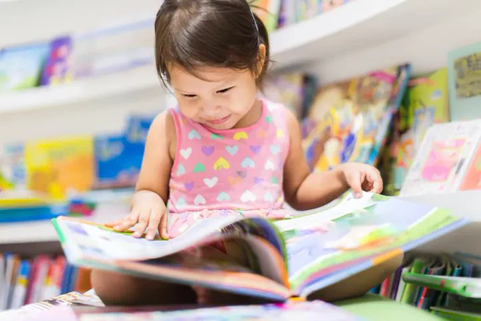 Picture of a little kid in a pink dress flipping through a picture book.