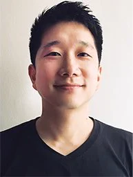 Profile photo of Anton Hur wearing a black v-neck shirt against a beige wall. Hur is a middle-aged Korean man with short black hair.